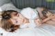 A woman laying on a bed with a white sheet.