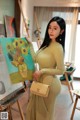 a woman in a yellow dress holding a painting