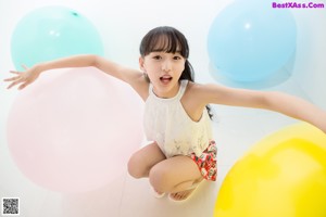 A little girl sitting on the floor with a bunch of balloons.