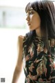 A woman with long black hair standing in front of a window.